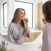 Woman in her 50s smiling while applying a Violaire purple whitening strip in a bright bathroom