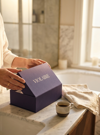 Hands opening a Violaire violet box on a marble counter beside an espresso — morning ritual